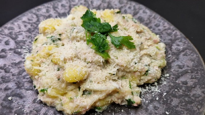 Assiette de gnocchi à la courgette crémeuse et au jambon saupoudré de parmesan et de quelques feuilles de persil.