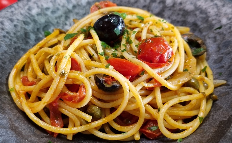 Assiette de spaghetti alla puttanesca avec tomates, anchois, olives noires, câpres, persil.