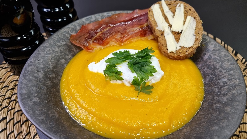 Assiette avec velouté de courge butternut accompagné de son œuf mollet, tranche de jambon cru grillé et tartine beurrée.